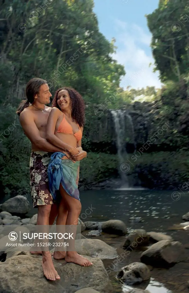 Couple Standing Together On Rock In Front Of Tropical Waterfall