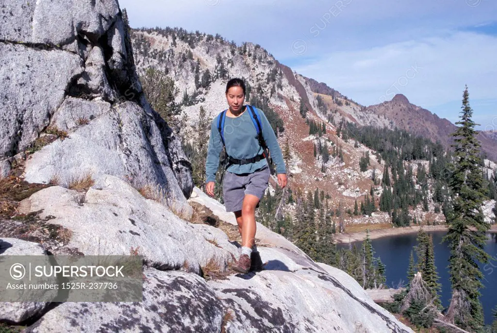 Female Hiker Walking Along A Steep Rocky Cliff Overlooking A Mountain Lake