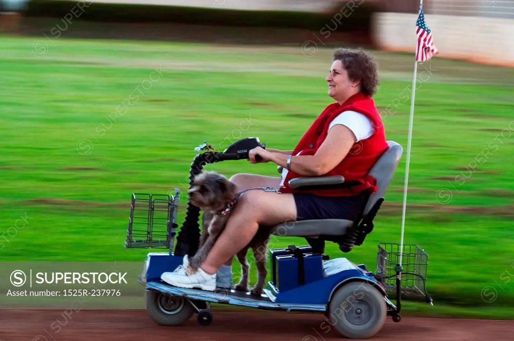 Caucasian Woman Driving A Motorized Cart With Her Dog And Sporting An American Flag