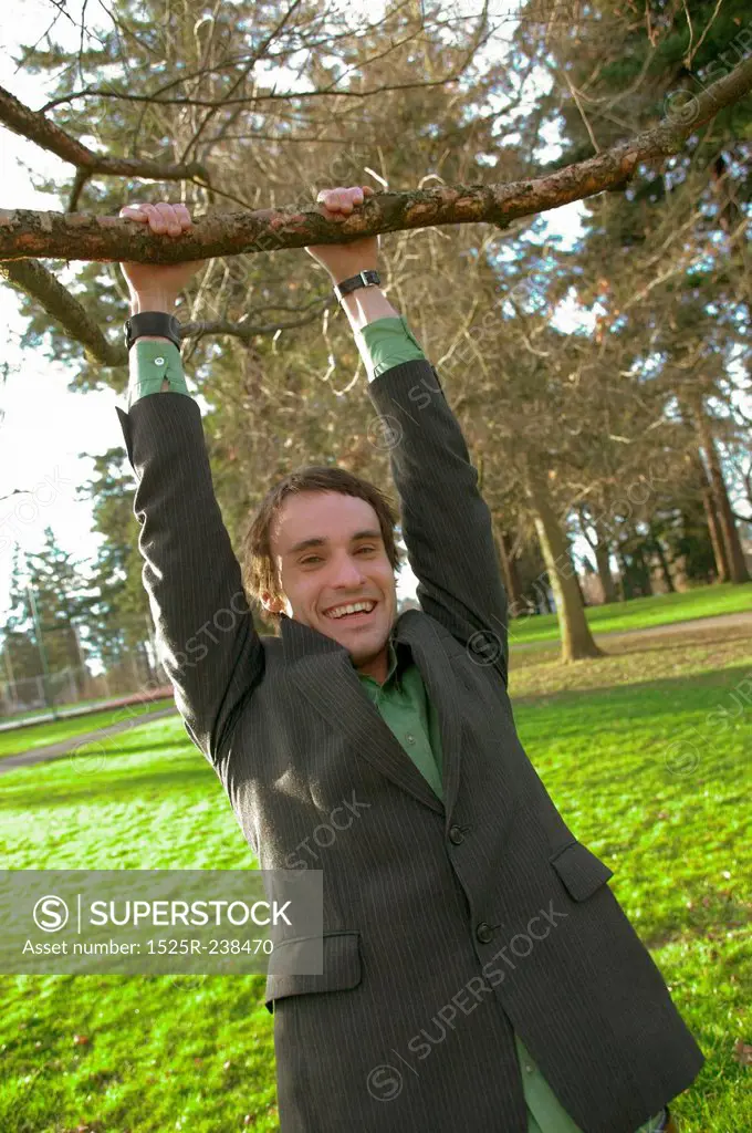 Twenty Something Male Hanging From A Tree Branch In The Park