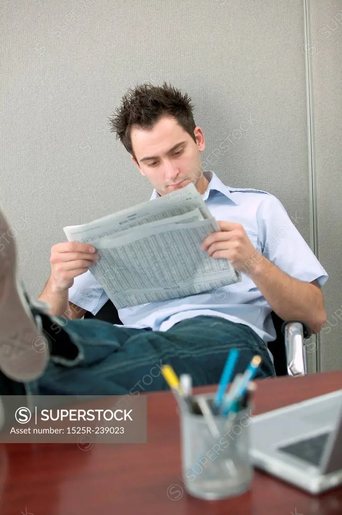 Young Man Reading Newspaper With Feet on Desk
