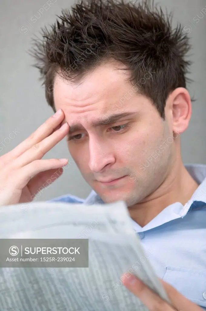 Young Man Reading Newspaper With Hand to Brow