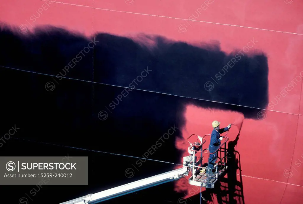 Construction worker on elevated platform spray painting wall