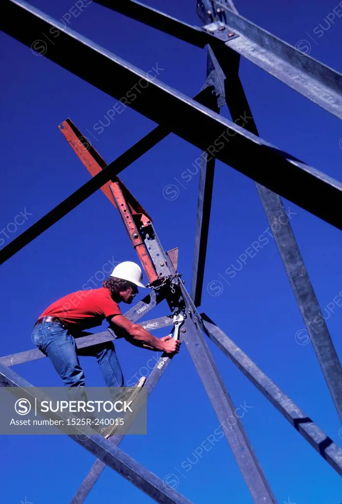 Construction worker on construction site balanced on girder using wrench to tighten metal supports