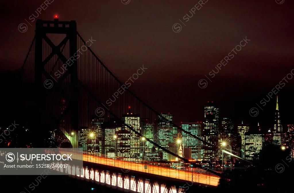 Suspension bridge at night with glowing urban cityscape in background