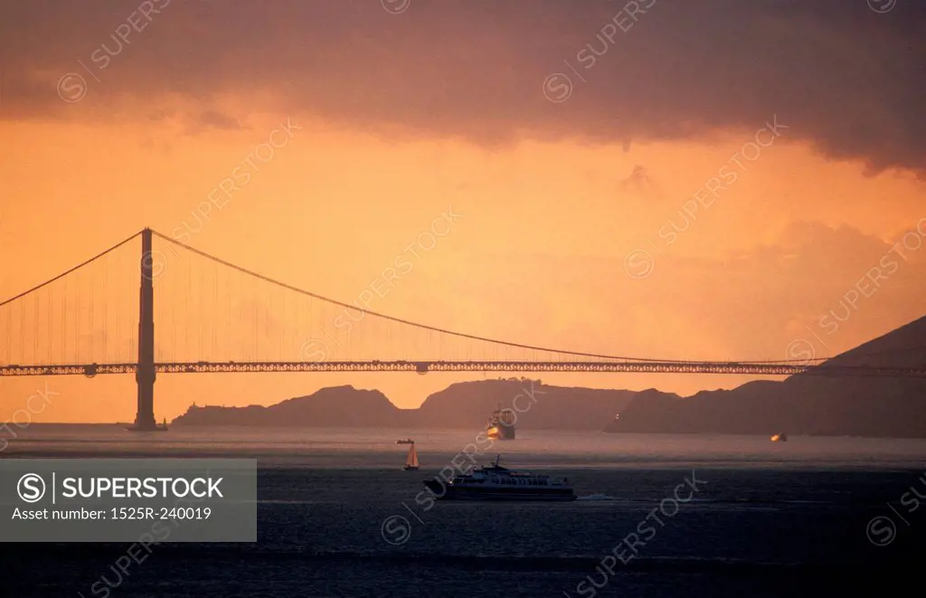 Silhouette of suspension bridge with boats in foreground