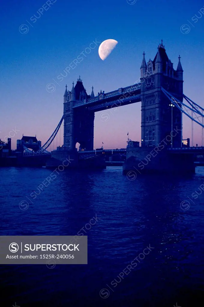 Silhouette of Tower Bridge and river with sunset and half moon in background, London, England