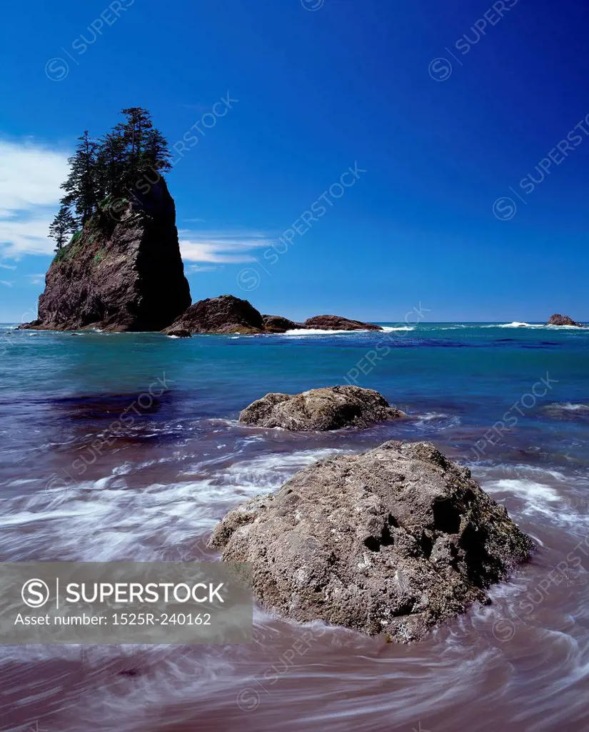 Swirling ocean water around rock with rock formation in background