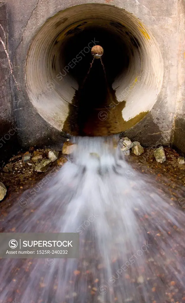 Blurred motion of water splashing out of cement sewer pipe