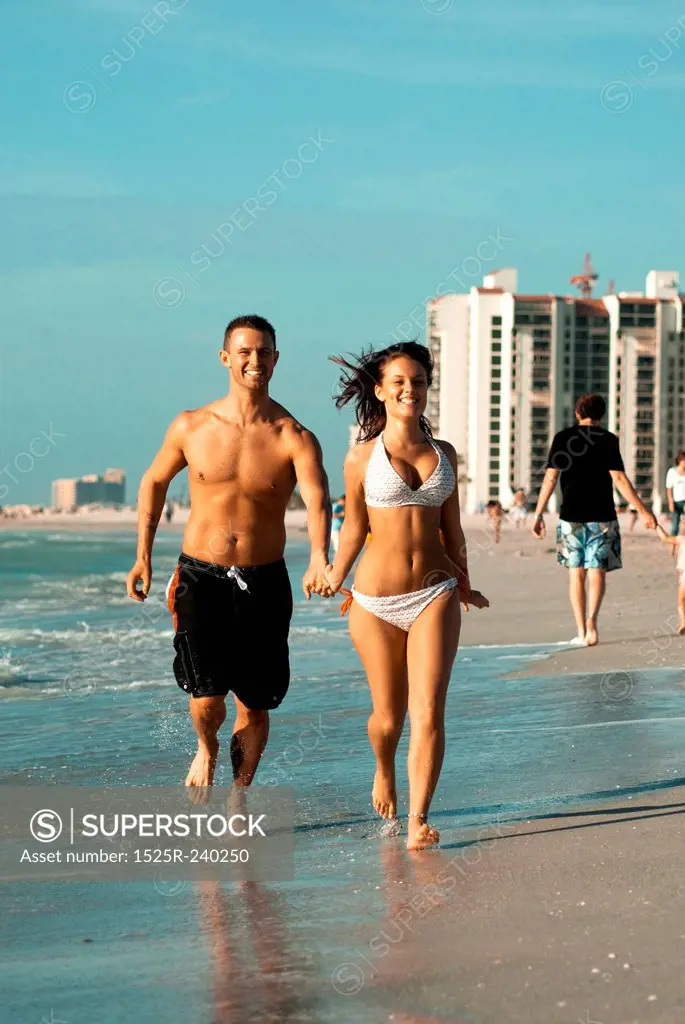 Couple in bathing suits holding hands and running on ocean beach while on vacation
