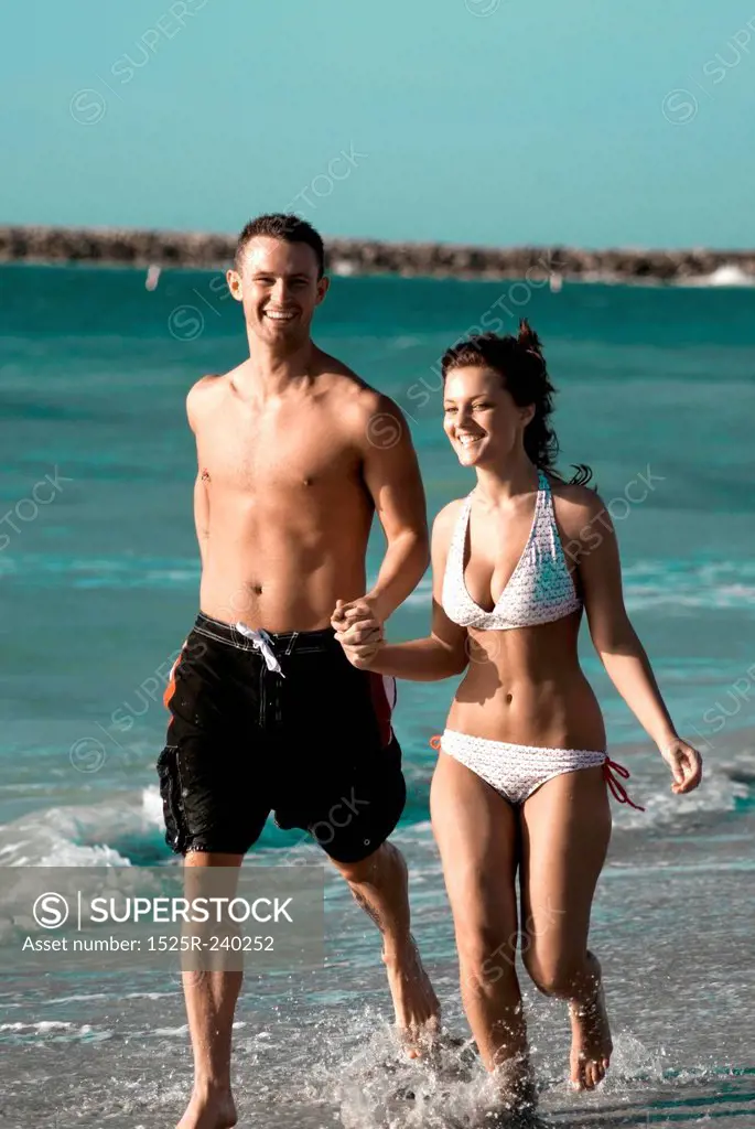 Couple in bathing suits holding hands and running on ocean beach while on vacation