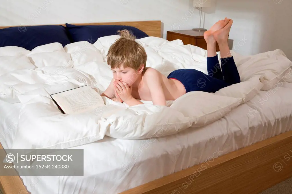 Bare chested boy laying on bed in bedroom reading book