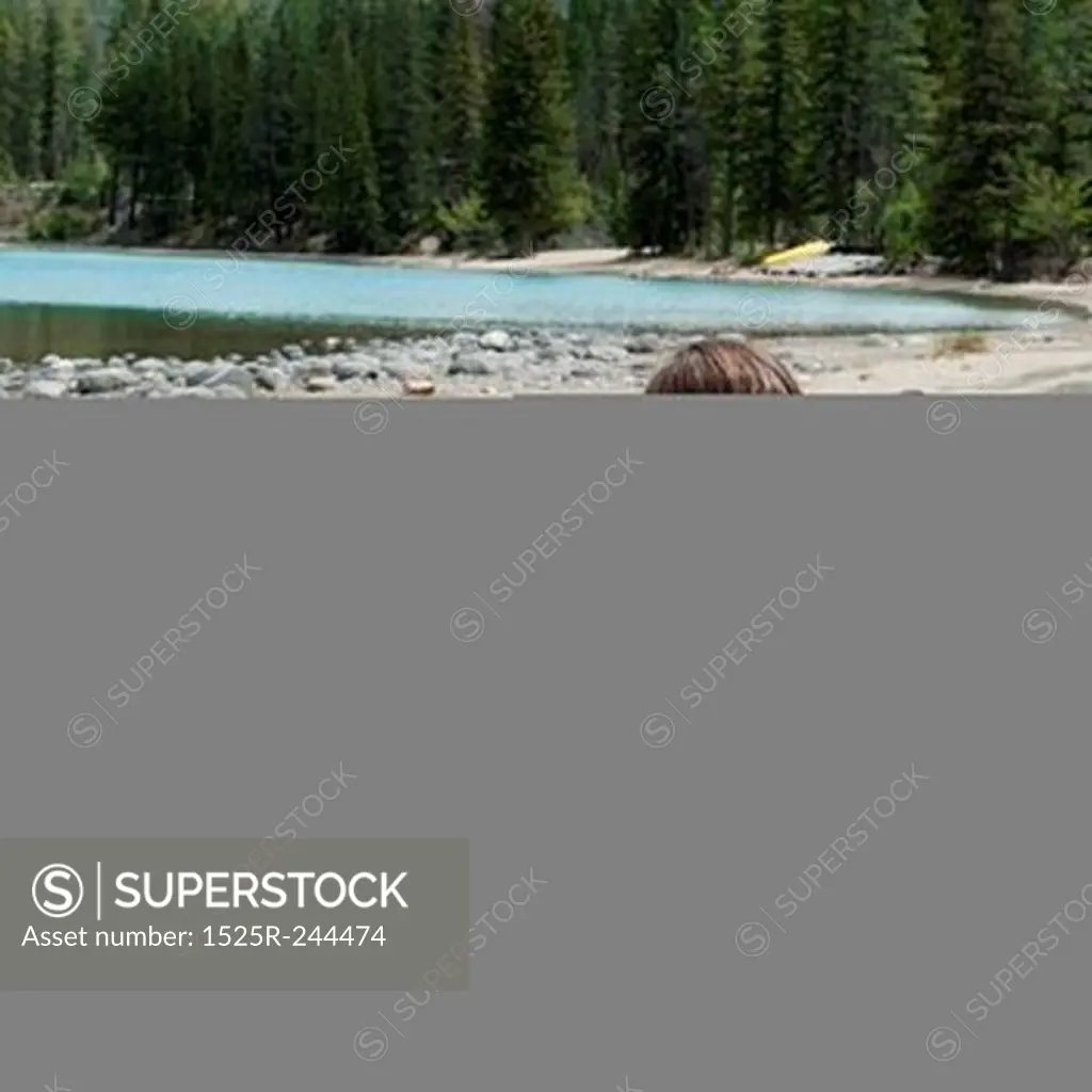 Girl sitting on sand at the lakeside, Edith Lake, Jasper National Park, Alberta, Canada