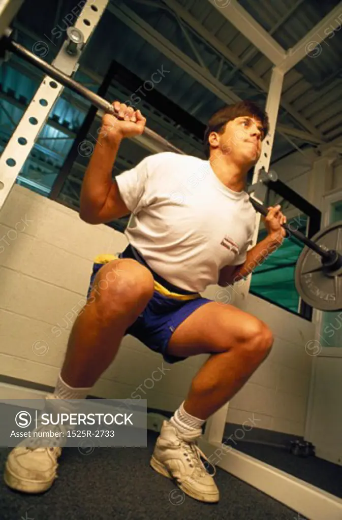 Low angle view of a young man lifting a bar bell in a gym