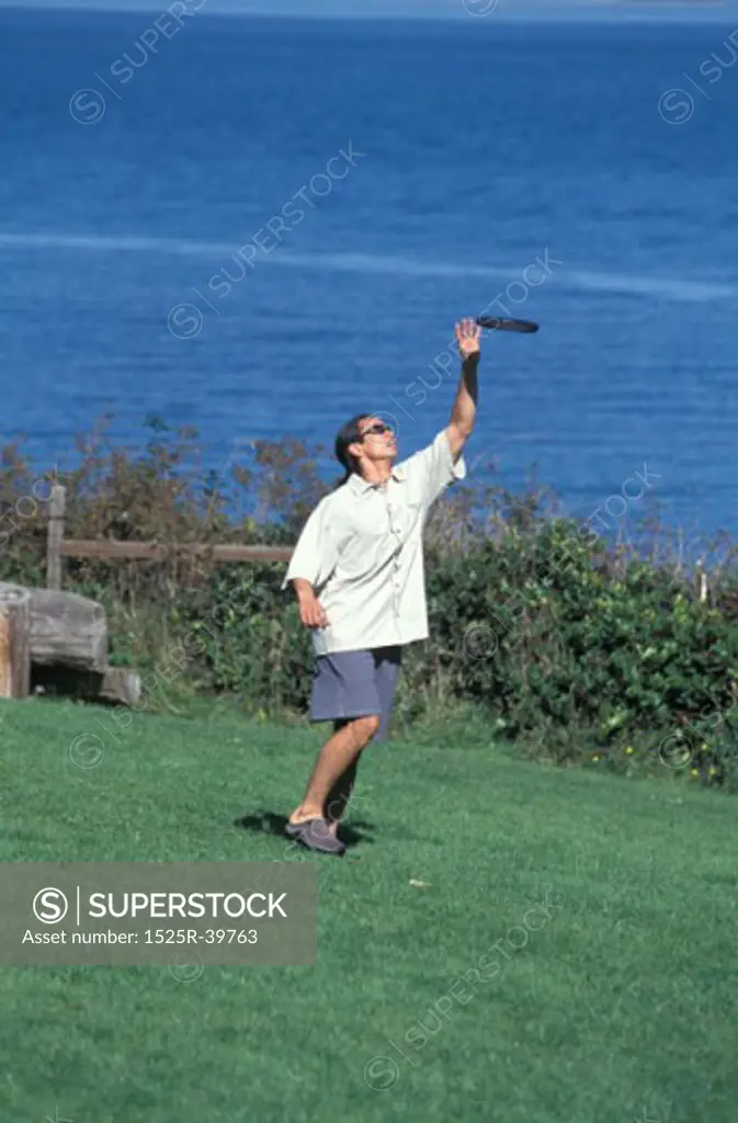 Asian American Man Catching A Frisbee Near A Lake