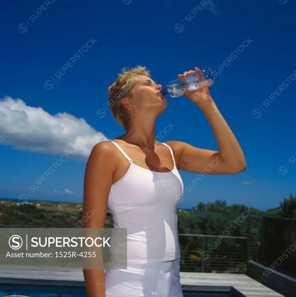 Young woman drinking water from a bottle at poolside