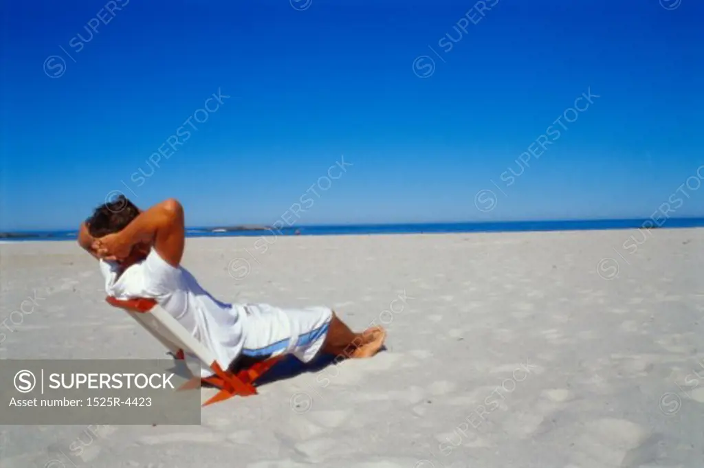 Side profile of a young man sitting on a chair on the beach