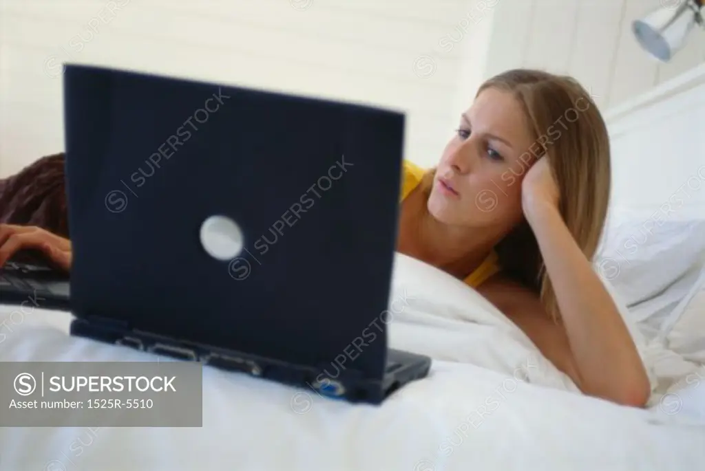 Young woman lying on the bed using a laptop