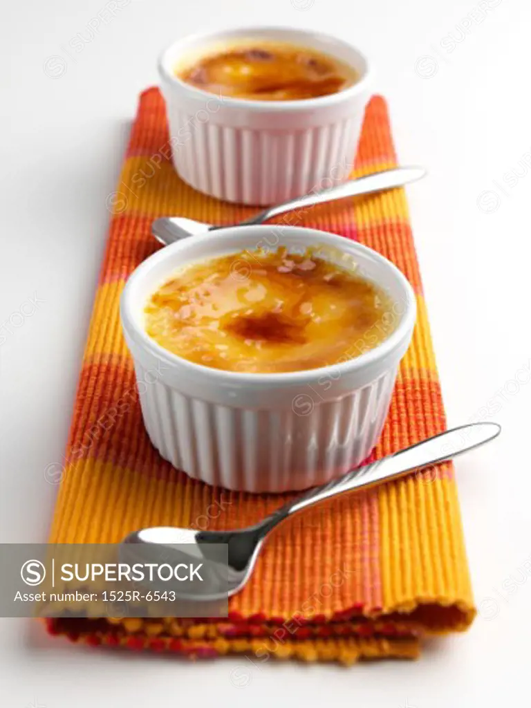 Close-up of two bowls of creme brulee with two spoons on a place mat