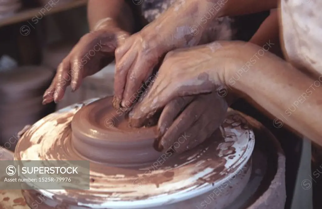 Two pairs of hands shaping clay on a potter's wheel