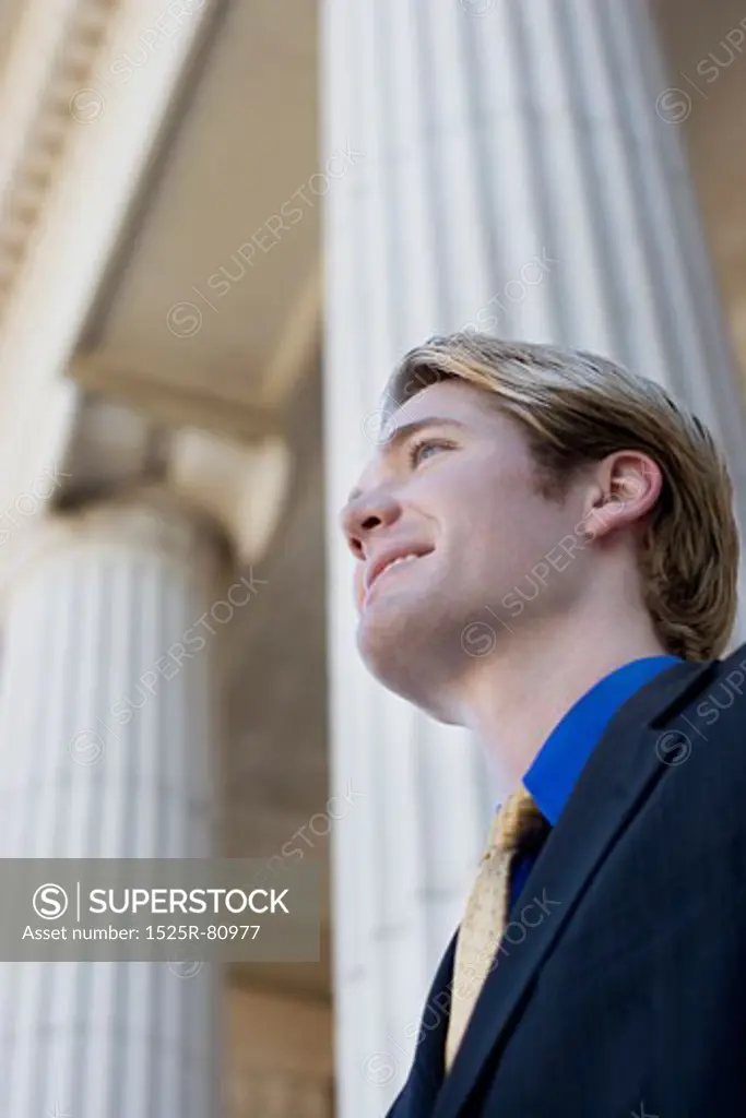 Businessman looks ahead and smiles as he stands in front of columns