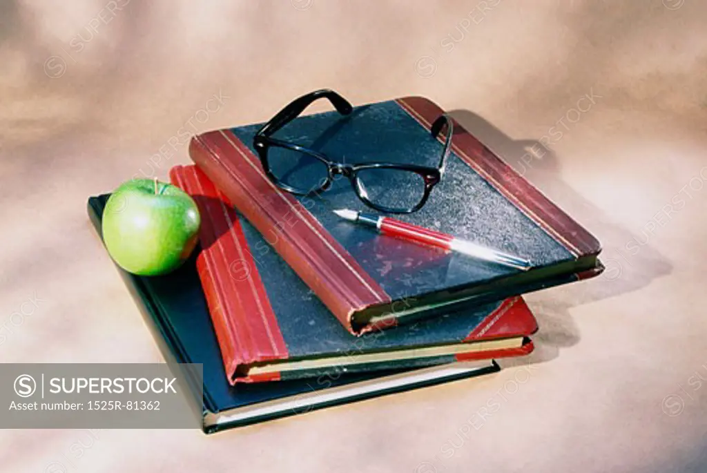 Granny Smith apple with a pen and eyeglasses on books