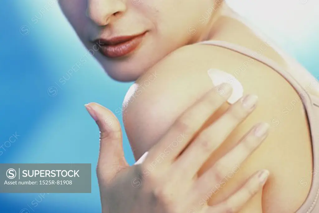 Close-up of a young woman applying moisturizer on her shoulder