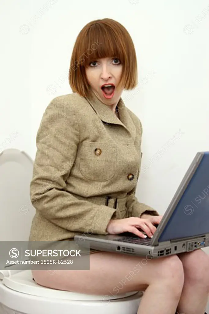 Businesswoman sitting on a toilet and working on a laptop