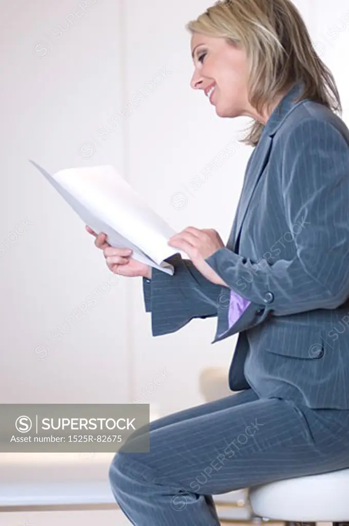 Businesswoman sitting on a stool and reading documents