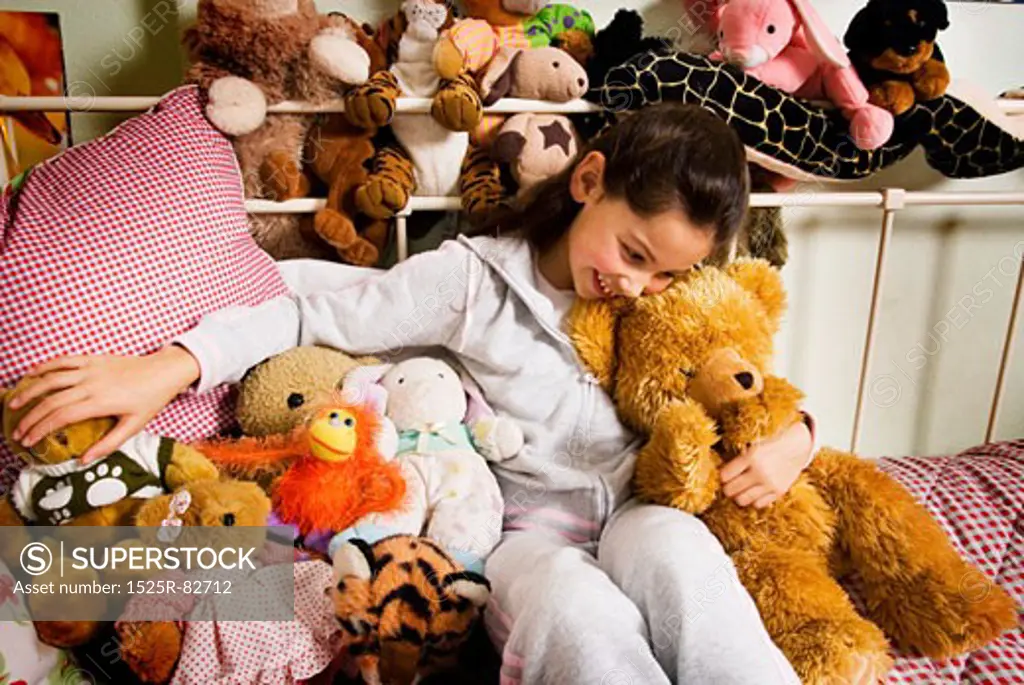 Girl playing with stuffed toys and smiling in a bedroom