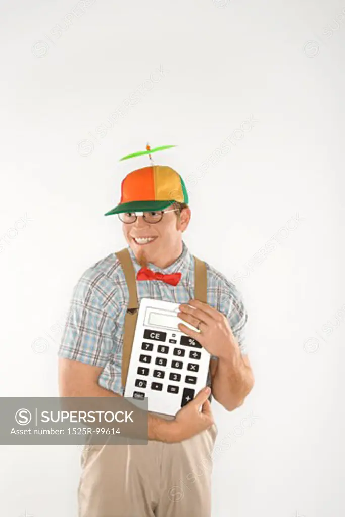 Caucasian young man dressed like nerd wearing beanie and smiling while holding large calculator.