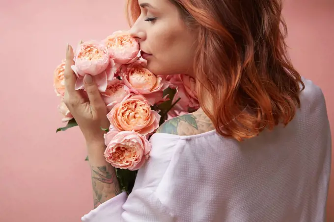 Beautiful girl with fragrant flowers on a background in a trendy color of the year 2019 Living Coral Pantone. Mother&rsquo;s Day and Valentine&rsquo;s Day greeting post cards.. A girl with a tattoo holds a bouquet of flowers roses on a pastel background in a trendy color of the year 2019 Living Coral Pantone. Congratulation card concept.