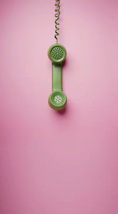 Green Vintage Retro Telephone Handset Hanfing on Pink background. Old Object from 1980-1990, Technology and Communication in the Past. Clean, Colourful  and Minimal