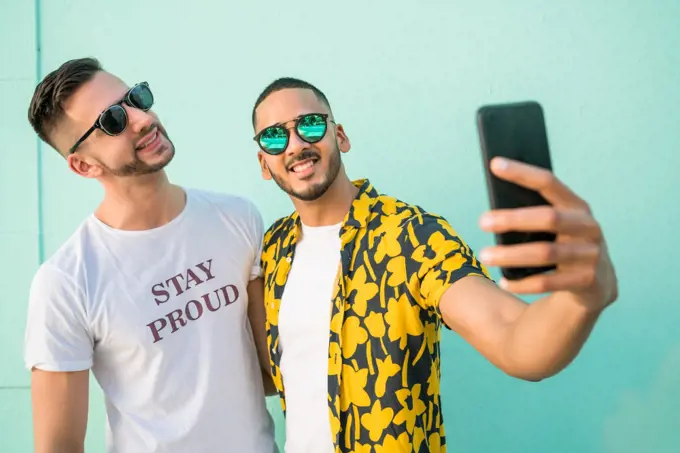 Portrait of happy gay couple spending time together and taking a selfie with mobile phone. Lgbt and love concept.
