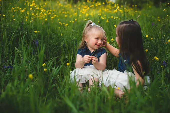Girls sitting in wildflower meadow face to face smiling