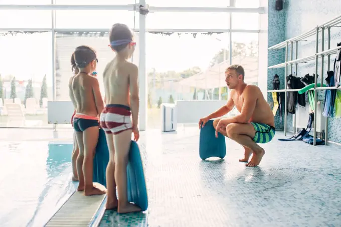Instructor training children in the pool. Boys with swimming goggles ready for swimming and stands near water. Healthy activity in pool. Sportive kids activity in modern sport center with pool.. Instructor training children in the pool