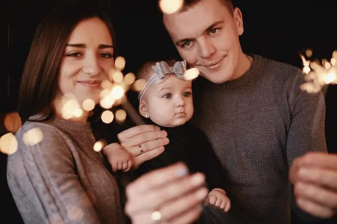 portrait of happy family, mom, dad and baby girl with sparklers and light. family in anticipation of Christmas. selective photo. portrait of happy family, mom, dad and baby girl with sparklers and light. family in anticipation of Christmas. selective photo.