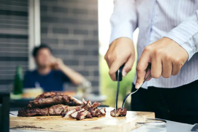 Asian friends are using a knife and a fork to cut the grilled meat on the chopping board to bring food together with friends celebrate with fun.