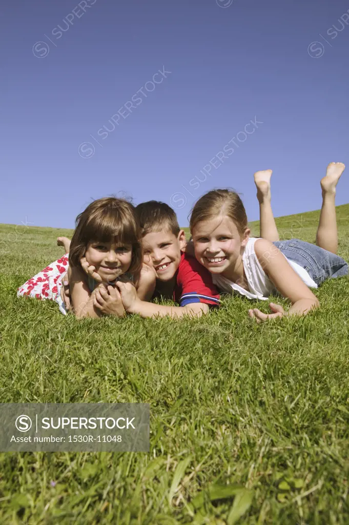 Three children lying on grassy hillside.