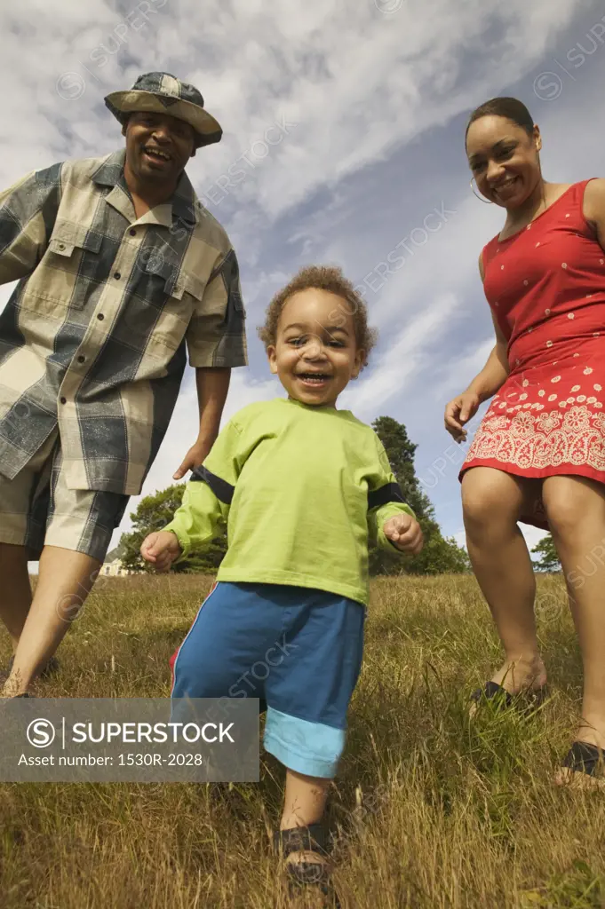 A couple playing with their son in a grassy field. 