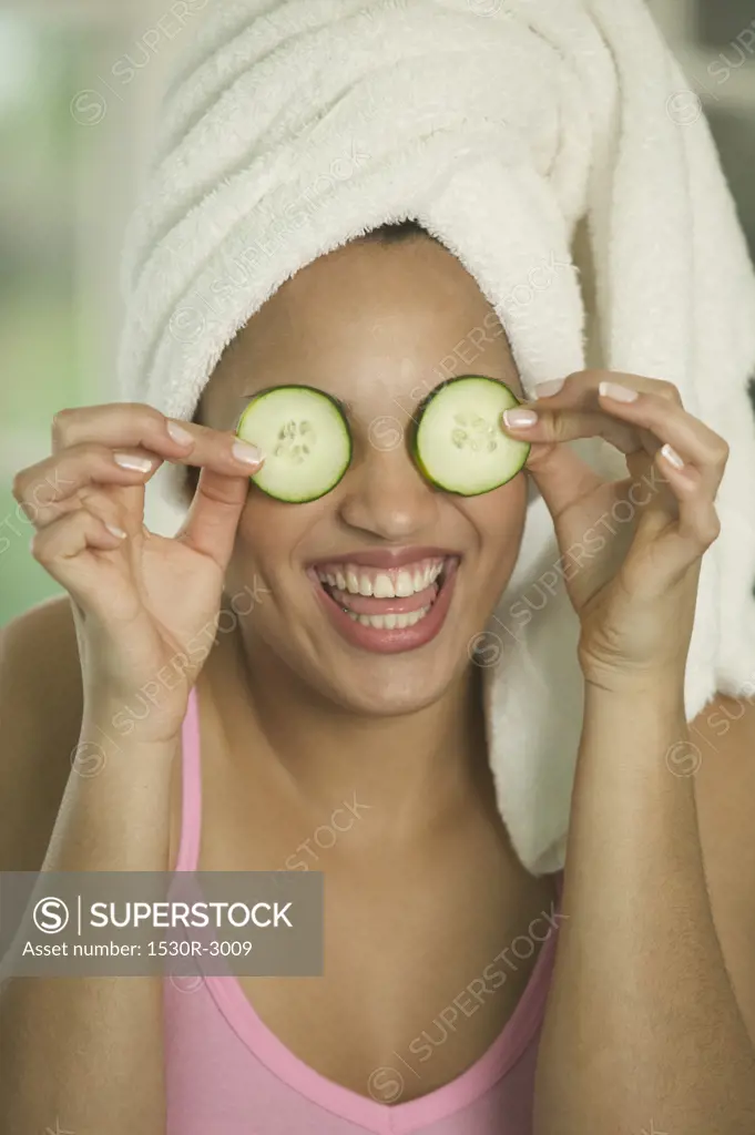 Woman holding cucumber slices over both eyes.