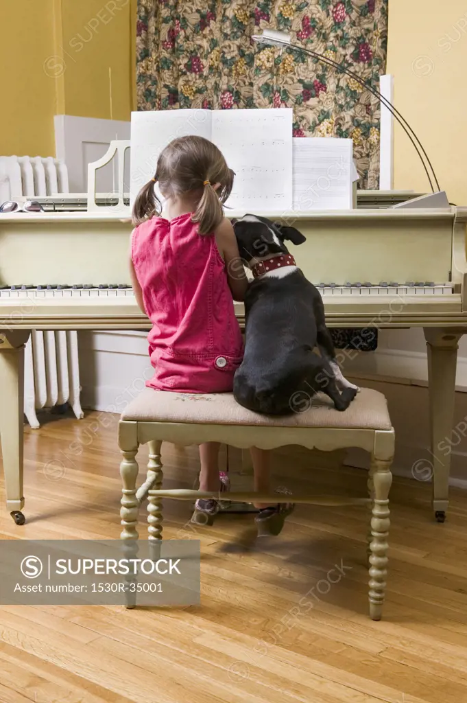 Girl and pet dog sitting on piano bench