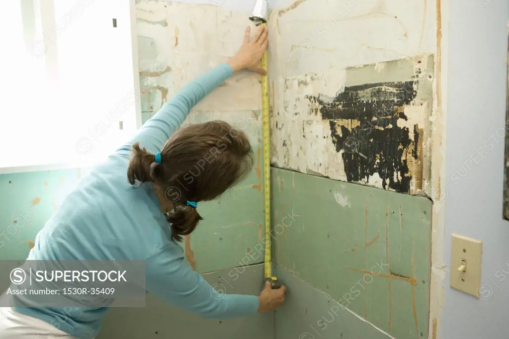 Woman measuring damaged shower wall