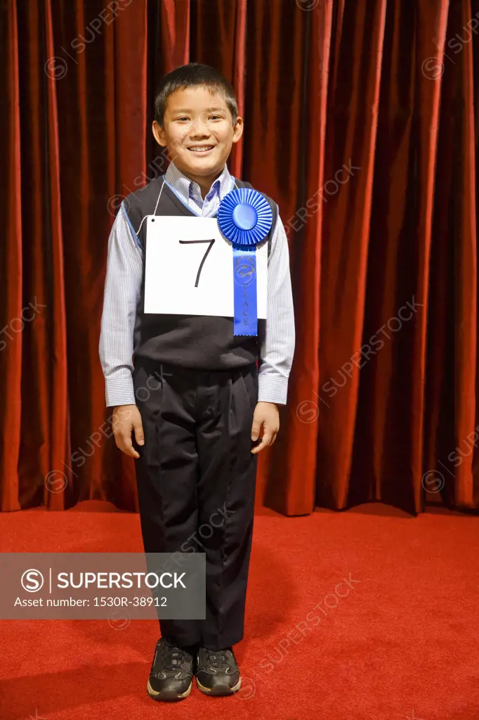 Asian boy wearing prize ribbon on stage
