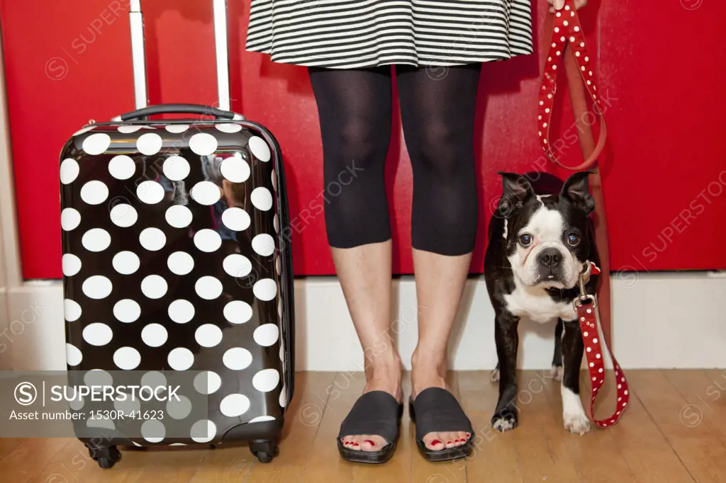 Woman with polka dot suitcase and dog on leash