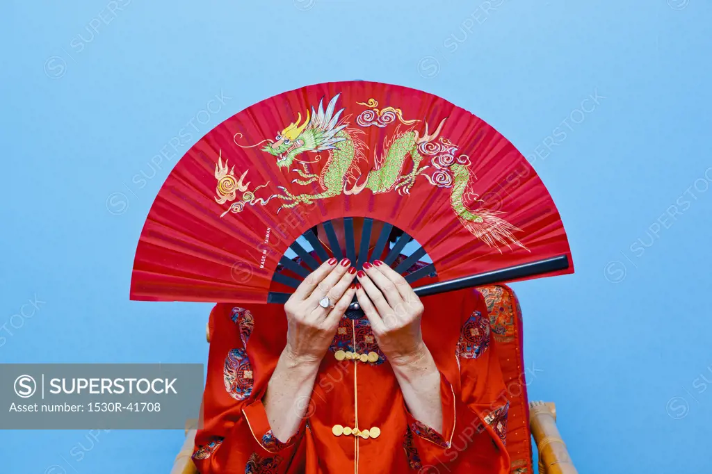 Woman holding red fan in front of her face,
