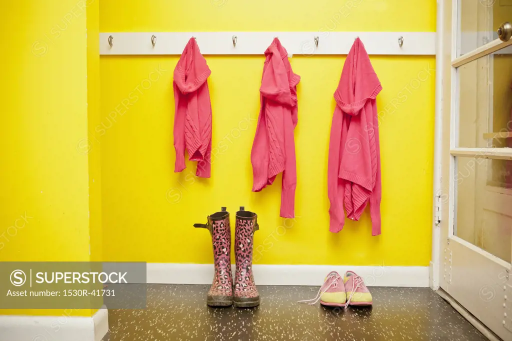 Sweaters on hooks with boots and shoes below,