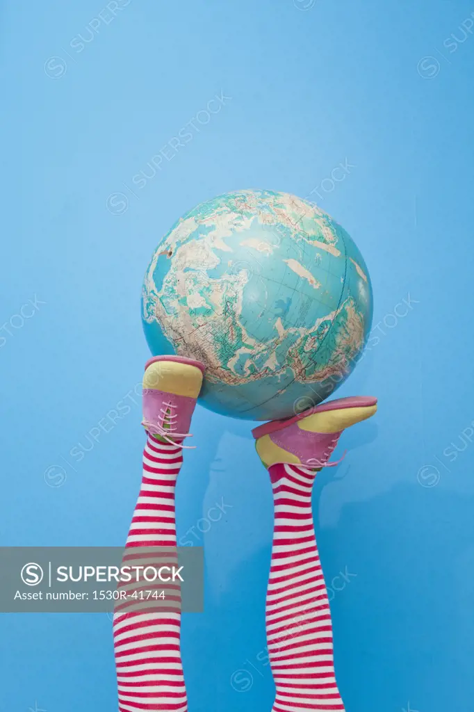 Legs in striped socks with colorful shoes holding globe,