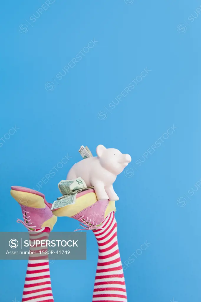 Legs in striped socks with colorful shoes holding piggy bank,