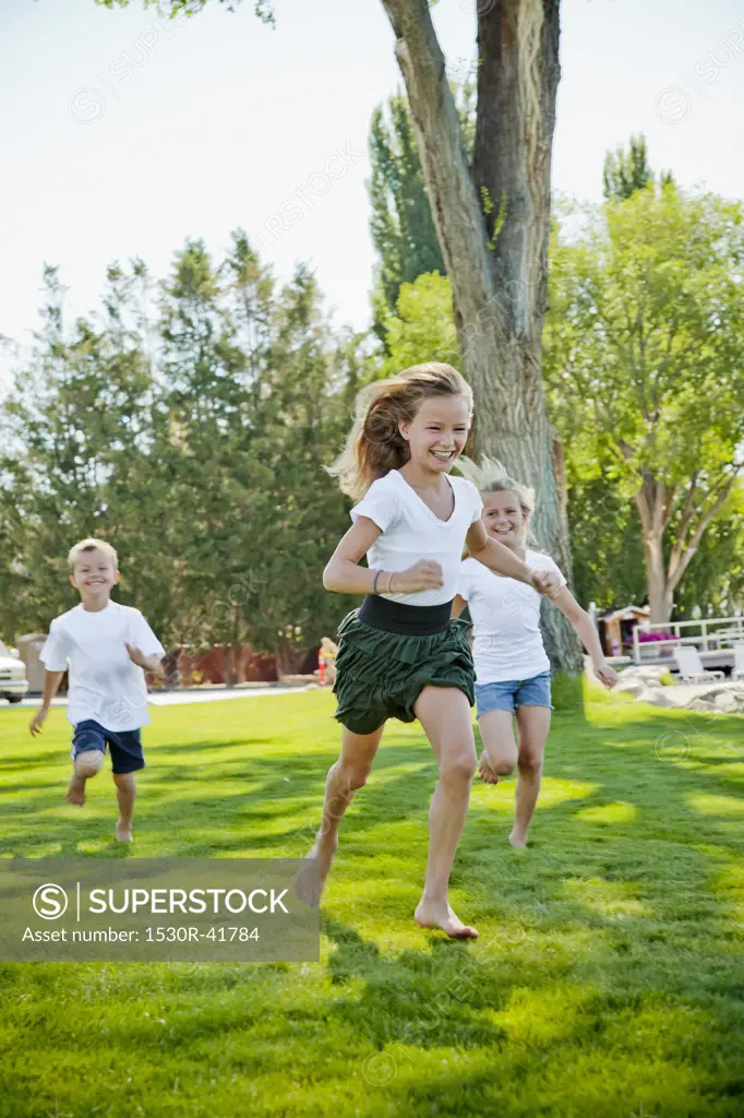 Three young children running in park,